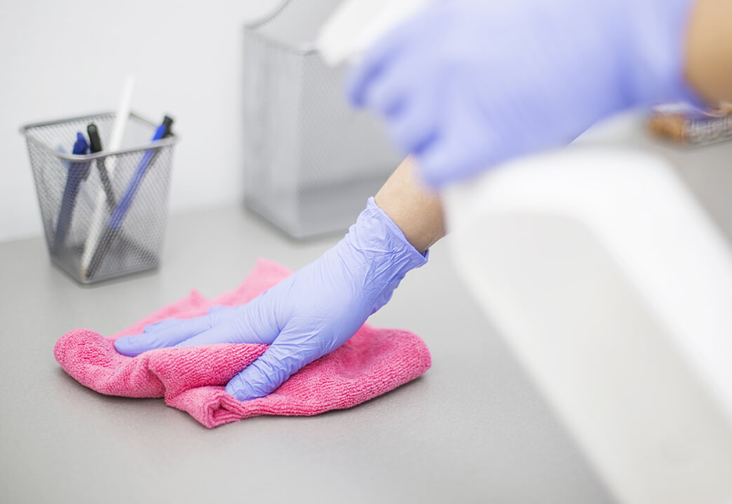 purple gloved hands cleaning a table with a pink cloth