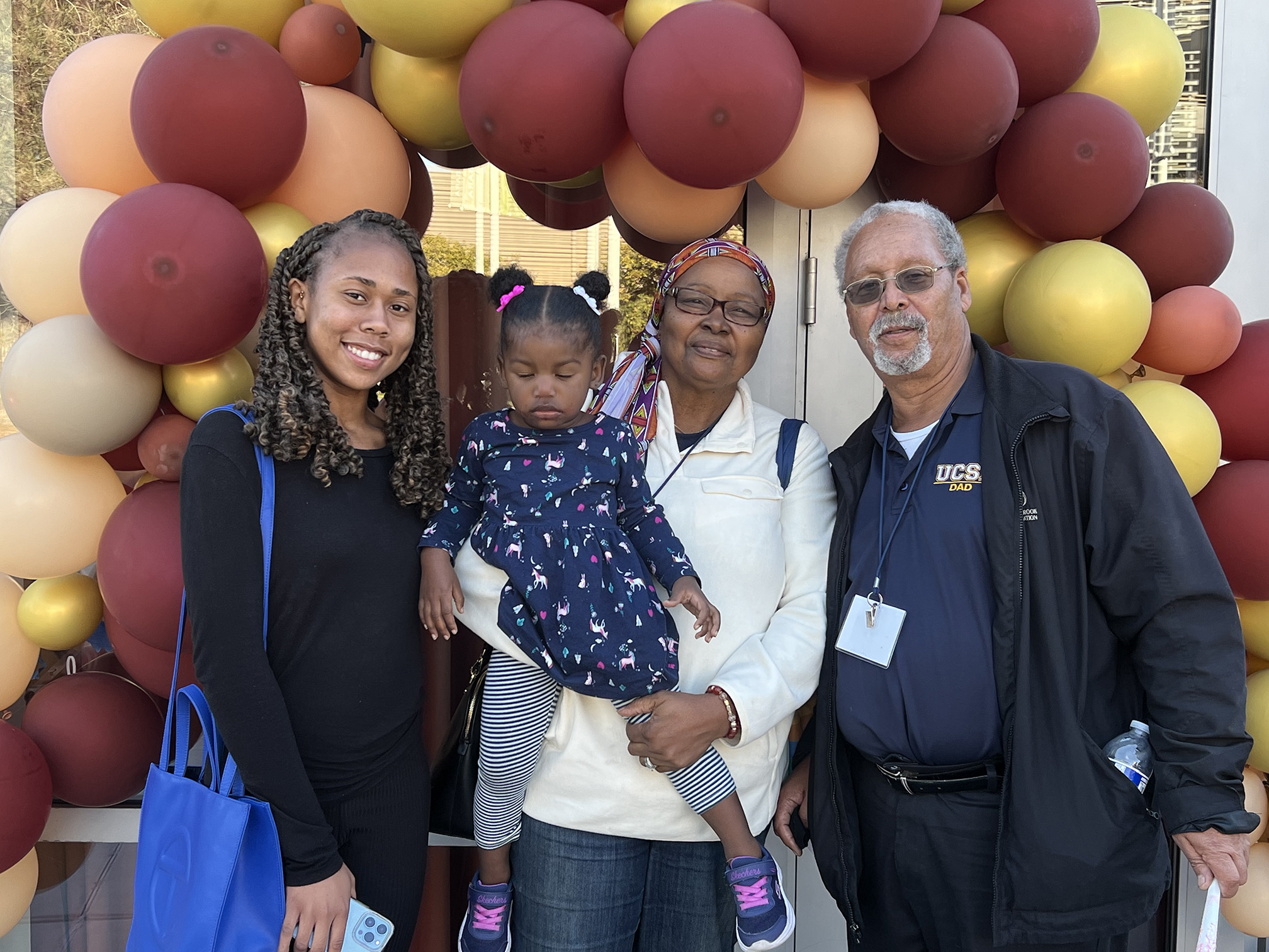 Family posing in front of yellow and re balloons