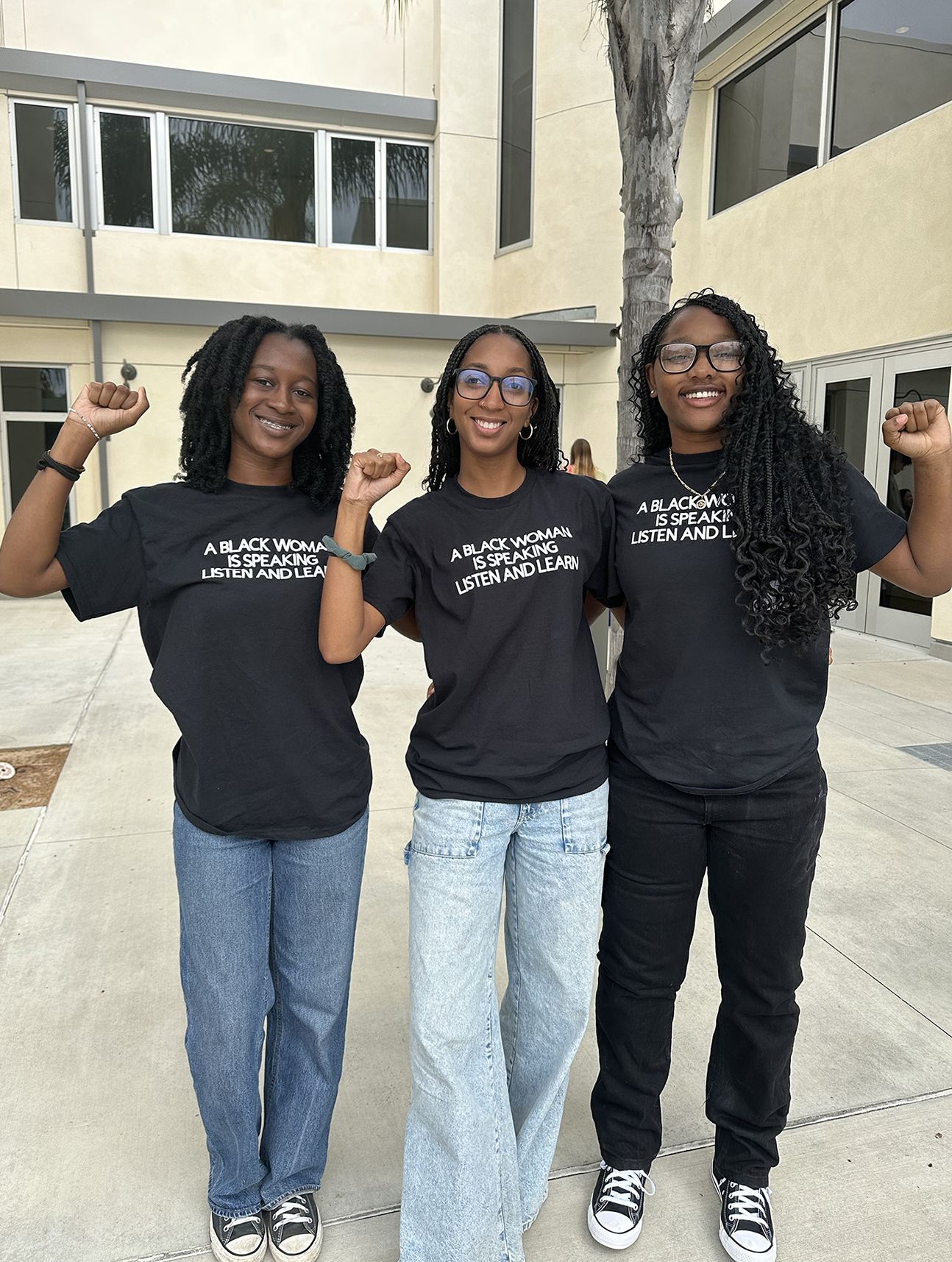 Group of 3 female students standing and showing "A Black Woman is Speaking BWHC T-shirt. Listen and Learn.hirt