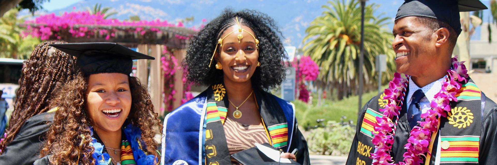 Close-up of two young women and one youn man wearing cap and gown at UCSB Black Graduation, outdoor on UCSB campus