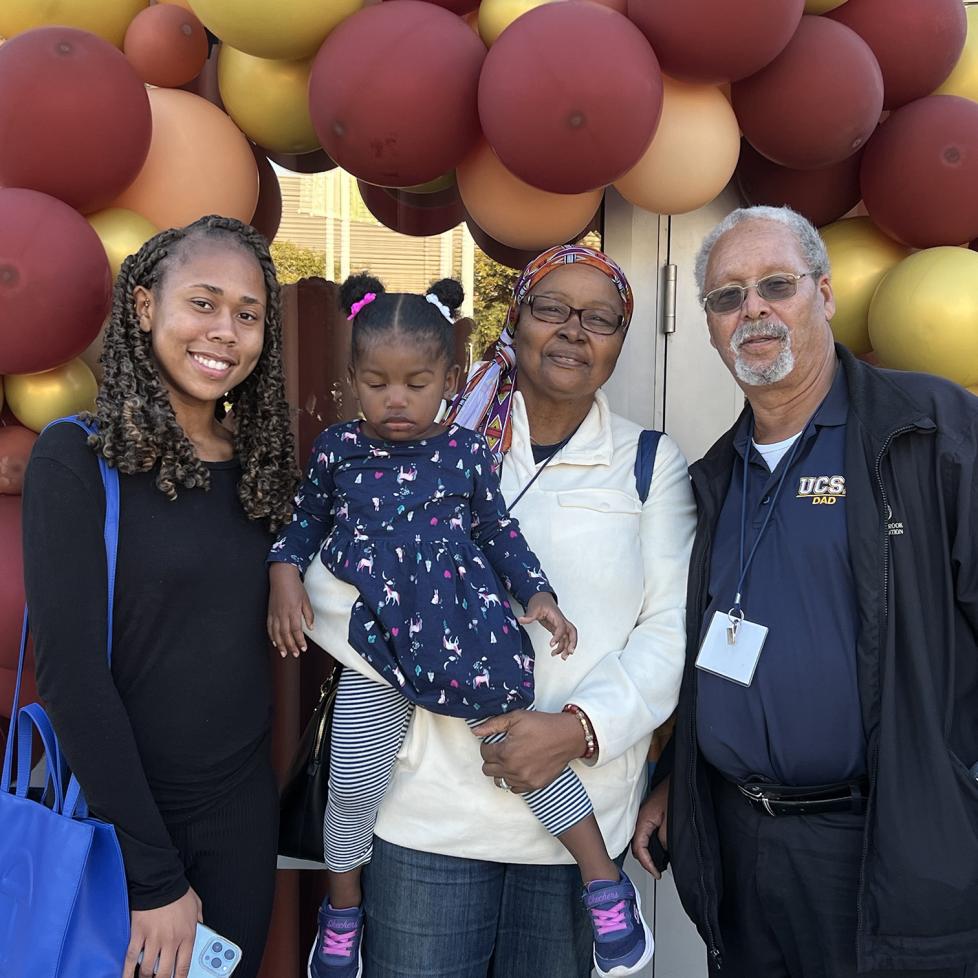 Family posing in front of yellow and re balloons